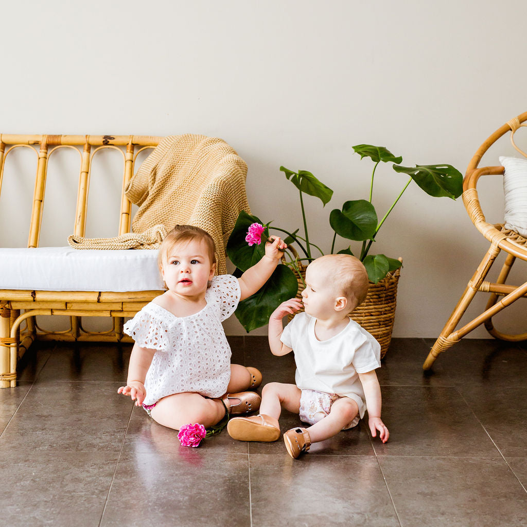 Two toddlers sitting next to each other wearing cloth nappies and one is holding a flower
