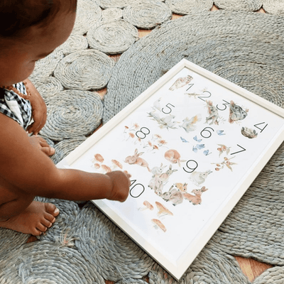 baby pointing at a  white framed art print featuring watercolour illustration of animals and numbers